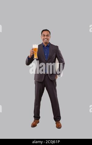 Homme d'affaires tenant le verre de bière. Homme d'affaires indien debout pleine longueur avec bière en main Banque D'Images