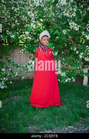 Reine dans la couronne et le manteau royal. Jolie fille sur le fond d'un jardin fleuri. Afro-américain en rouge Banque D'Images