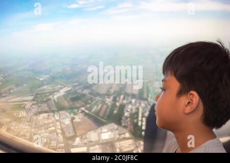 Portrait asiatique garçon a regardé la vue à l'extérieur de la fenêtre de l'avion Background City et la vue du ciel Banque D'Images