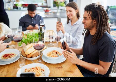 Groupe de personnes qui mangent ensemble à la table regarde sur smartphone avant le début et prend des photos de gourmets Banque D'Images