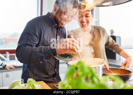 Des amis heureux ou un couple cuisant de la nourriture dans la cuisine pour le repas ensemble Banque D'Images