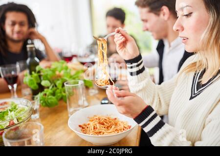 Femme mangeant des spaghetti avec de la sauce tomate avec des amis à la table de salle à manger tout en ayant repas ensemble Banque D'Images