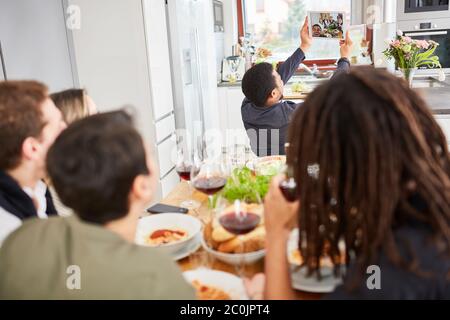 Homme avec des amis à table dîner ensemble fait des appels vidéo ou selfie avec une tablette Banque D'Images