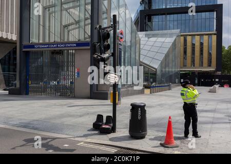 Une femme policière signale par radio les dégâts causés par une circulation et une lumière piétonne écrasées qui ont été heurtées par un bus à impériale de Londres et qui l'a laissé osciller dangereusement dans le vent, et qui ont laissé les lumières à cette intersection avec Charing Cross Road, Tottenham court Road et New Oxford Street, le 11 juin 2020, à Londres, en Angleterre. Banque D'Images