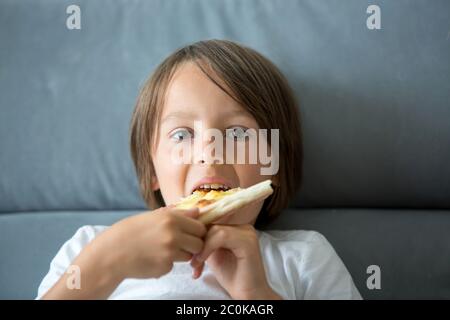 Une petite pizza de race blanche. Enfant affamé prenant un morceau de pizza lors d'une fête de pizza. Enfant taché Banque D'Images