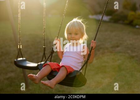 Enfant doux, balançant sur une balançoire dans le jardin au coucher du soleil, souriant heureux Banque D'Images