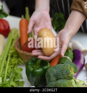 Vue rapprochée des mains tenant les jeunes pommes de terre tout en se tenant à table avec d'autres légumes frais de la ferme Banque D'Images