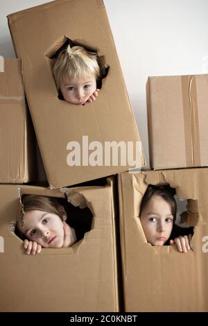 Enfants doux, frères garçons, cachette dans une boîte en carton, regarder dehors, isolé. Enfants tristes, rester à la maison pour cause de quarantaine, jouer ensemble Banque D'Images