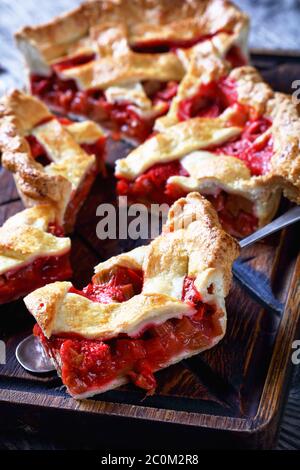 Gros plan de tranches de Rhubarb maison fraîchement cuites aux fraises sur une planche à découper et sur une pelle à gâteau sur une table en bois, vue verticale Banque D'Images