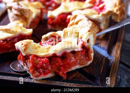Gros plan d'une tranche de fraise maison fraîchement cuite Rhubarb Pie sur une pelle à gâteau sur une planche à découper en bois, vue sur le paysage Banque D'Images