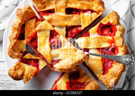 Gros plan de tranches de rhubarbe maison fraîchement cuites aux fraises sur une assiette à gâteau blanche sur une table en bois, plat, Banque D'Images