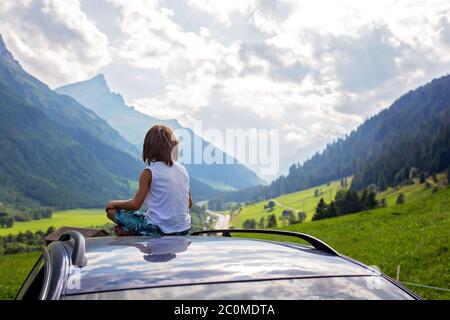 Enfant mignon, garçon assis sur un plafond de voiture, méditant en appréciant le calme de la nature, voyage sur la route vers les montagnes pittoresques, l'été Banque D'Images