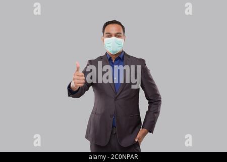 Homme d'affaires montrant Thoump Up portant un masque médical et des gants isolés. Panneau Indian Business Man Standing Thump Up Banque D'Images
