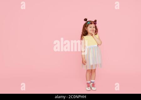 Portrait de petite fille surprise dans des lunettes de soleil sur fond rose. Modèle enfant ont plaisir et saut. Publicité des produits pour enfants Banque D'Images