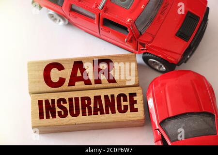 Mots d'assurance automobile sur des blocs de bois et deux voitures rouges dans un accident de la route sur fond blanc. Concept d'assurance Banque D'Images