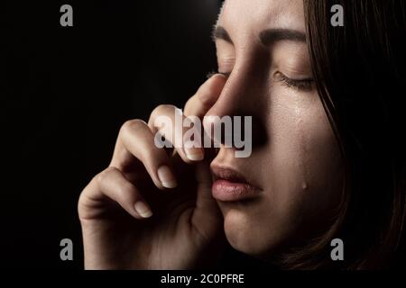 triste femme avec les yeux fermés pleurant, sur fond noir, portrait de gros plan, vue latérale Banque D'Images