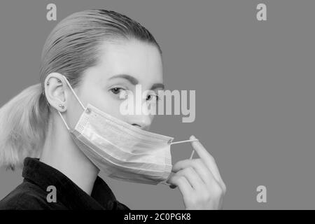 jeune femme en masque médical de protection regardant l'appareil photo sur fond gris Banque D'Images