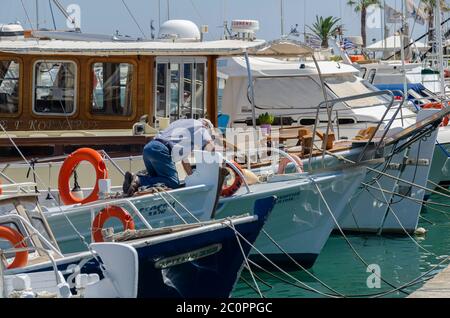 Héraklion, Crète / Grèce. Vue sur le port de plaisance de la ville d'Héraklion, où les bateaux de pêche et les yachts sont amarrés. Un homme effectue des travaux d'entretien sur son bateau Banque D'Images