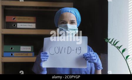 Le médecin porte l'inscription Covid-19. La femme médique en uniforme protecteur montre un slogan sur l'épidémie dangereuse de virus. Concept de santé Banque D'Images