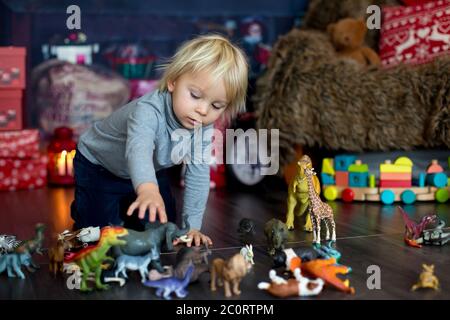 Doux blond tout-petit garçon, jouant avec des animaux en plastique et des dinosaures à la maison, décoration de noël autour de lui Banque D'Images