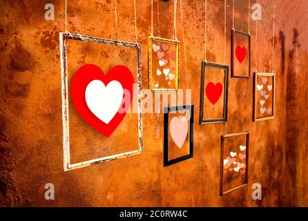Coeurs dans de vieux cadres et suspendus par le vieux fond de mur orange, montrant votre concept de jour d'Amour et de Saint Valentin Banque D'Images