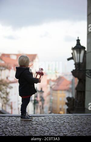 Magnifique enfant avec lanterne et ours en peluche, habillé à la mode, regardant la vue de nuit de Prague ville, l'hiver Banque D'Images