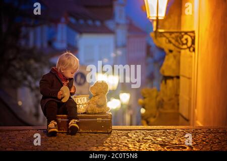 Magnifique enfant avec lanterne et ours en peluche, habillé à la mode, regardant la vue de nuit de Prague ville, l'hiver Banque D'Images