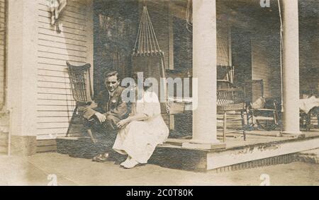 Photographie antique d'avril 1913, homme et femme assis sur le porche extérieur. Emplacement exact inconnu, probablement New Hampshire ou Massachusetts. SOURCE : PHOTO ORIGINALE Banque D'Images