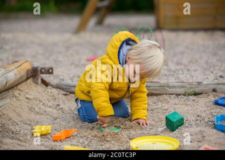 Petit enfant blond en blonde, blouson jaune, jouant sur le terrain de jeu, jour ensoleillé d'automne Banque D'Images