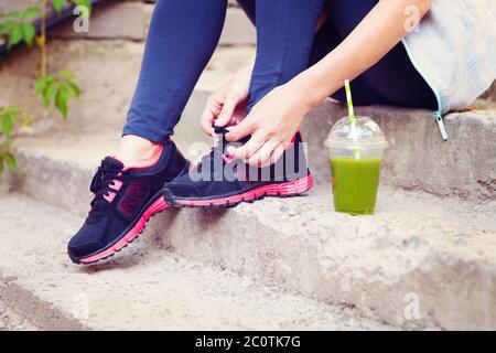 Coupe smoothie Detox verte et femme laçage des chaussures de course avant l'entraînement Banque D'Images