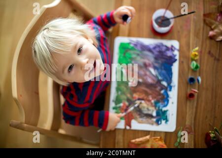 Un tout-petit garçon doux avec un tablier rouge, peint à la maison avec des couleurs d'eau Banque D'Images