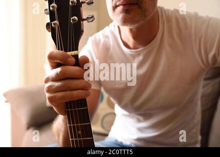 Gros plan de l'homme en t-shirt blanc à manches courtes, prenant la guitare acoustique par le cou Banque D'Images