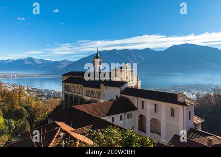 Vue panoramique imprenable sur l'église Madonna del Sasso au-dessus de la ville de Locarno avec le lac majeur, la montagne enneigée des Alpes suisses et le ciel bleu nuage à l'arrière Banque D'Images