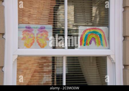 Dessins d’un arc-en-ciel et d’un papillon pour enfants, avec le message “Stay safe”, affichés dans la fenêtre d’une maison. La pandémie du coronavirus. Angleterre. Banque D'Images