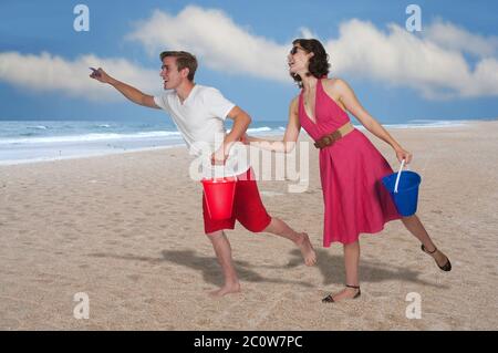 Couple qui court avec un seau de sable Banque D'Images