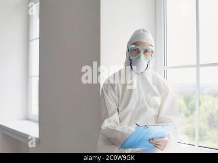 Médecin ou chercheur médical portant un masque facial et un vêtement de protection du corps avec un presse-papiers. Banque D'Images