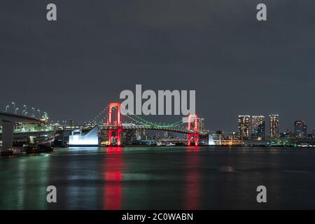 Vue nocturne du pont Rainbow, illuminé en rouge comme un signe de 'Tokyo Alert (alerte de coronavirus pour la région de Tokyo)' à Odaiba, Japon. Banque D'Images