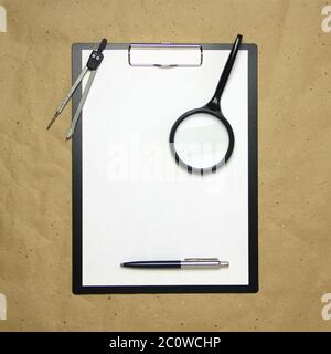 Une tablette avec une feuille blanche au format A4 avec loupe, stylo et séparateur sur papier beige. Concept d'analyse, d'étude, de travail attentif. Photo avec un emplacement vide pour votre texte et votre dessin. Banque D'Images