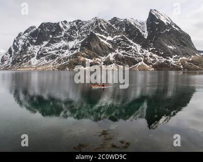 Deux kayakistes pagayez à travers un reflet de montagne sur Reinefjorden. Banque D'Images