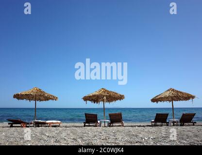 Des chaises longues sous des palmiers laissent des parasols sur la plage de l'île de Samos, en Grèce Banque D'Images