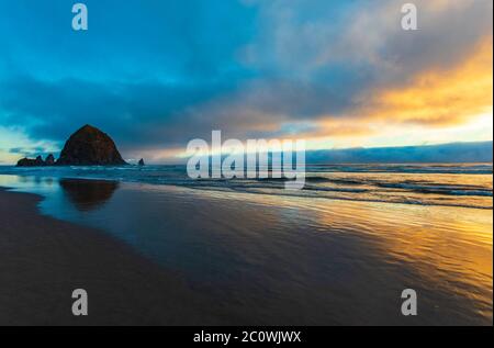 En regardant la plage de Cannon vers Haystack Rock, qui se reflète dans l'eau au coucher du soleil le long de la côte de l'Oregon Banque D'Images