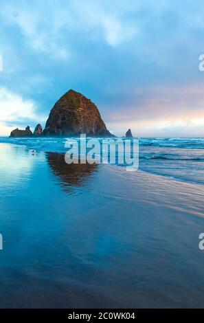 Image verticale - pile géante de la mer Haystack Rock se reflétant dans l'eau au coucher du soleil sur la plage de Cannon en Oregon Banque D'Images