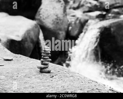 Pyramide de galets équilibrée avec cascade de rivière non concentrée sur fond . Image en noir et blanc. Banque D'Images