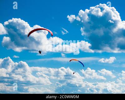 Deux silhouettes de parapente sombre sur fond de ciel bleu d'été et de nuages blancs. Thème sport adrénaline. Banque D'Images