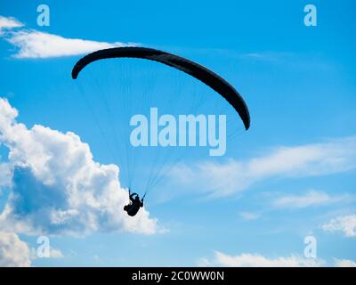 Silhouette de parapente sombre sur fond de ciel bleu d'été et de nuages blancs. Thème sport adrénaline. Banque D'Images