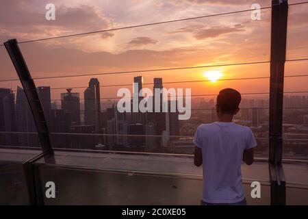 Jeune homme observant le coucher de soleil sur la ligne d'horizon du centre-ville de Singapour depuis la terrasse du Marina Bay Sands Hotel. Singapour Banque D'Images