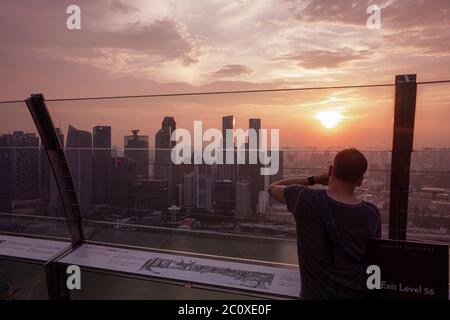 Jeune homme observant le coucher de soleil sur la ligne d'horizon du centre-ville de Singapour depuis la terrasse du Marina Bay Sands Hotel. Singapour Banque D'Images