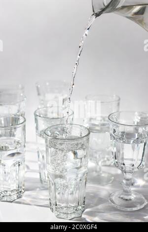 La main verse de l'eau fraîche d'un décanter dans un fond en verre, clair. Gros plan, vertical. Banque D'Images