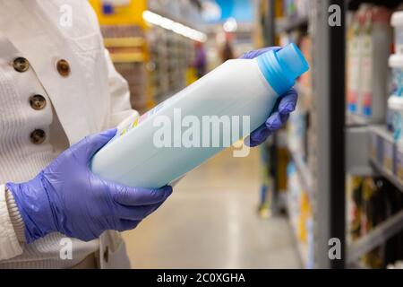 Femme porte des gants médicaux de protection en caoutchouc, choisit des produits chimiques domestiques, désinfectant pour la maison dans le supermarché, gros plan. Mesures de protection contre Banque D'Images