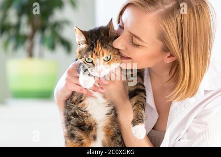 Gros plan de femme souriante dans une chemise blanche embrassant, embrassant, embrassant avec tendresse et amour chat domestique à la maison. Amour pour les animaux, animaux de compagnie concept Banque D'Images